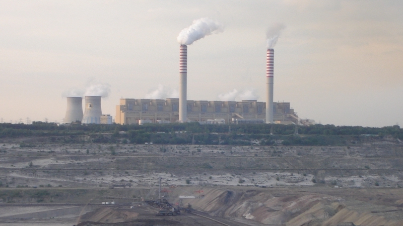 large coal plant with mine in foreground, smoke coming out of stacks, dark gray sky