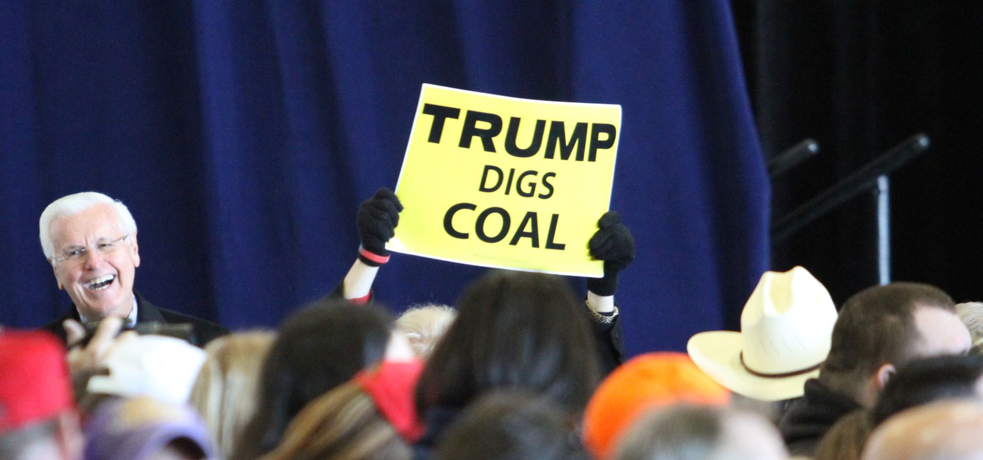 a Trump supporter holding up a "trump digs coal" sign at a rally