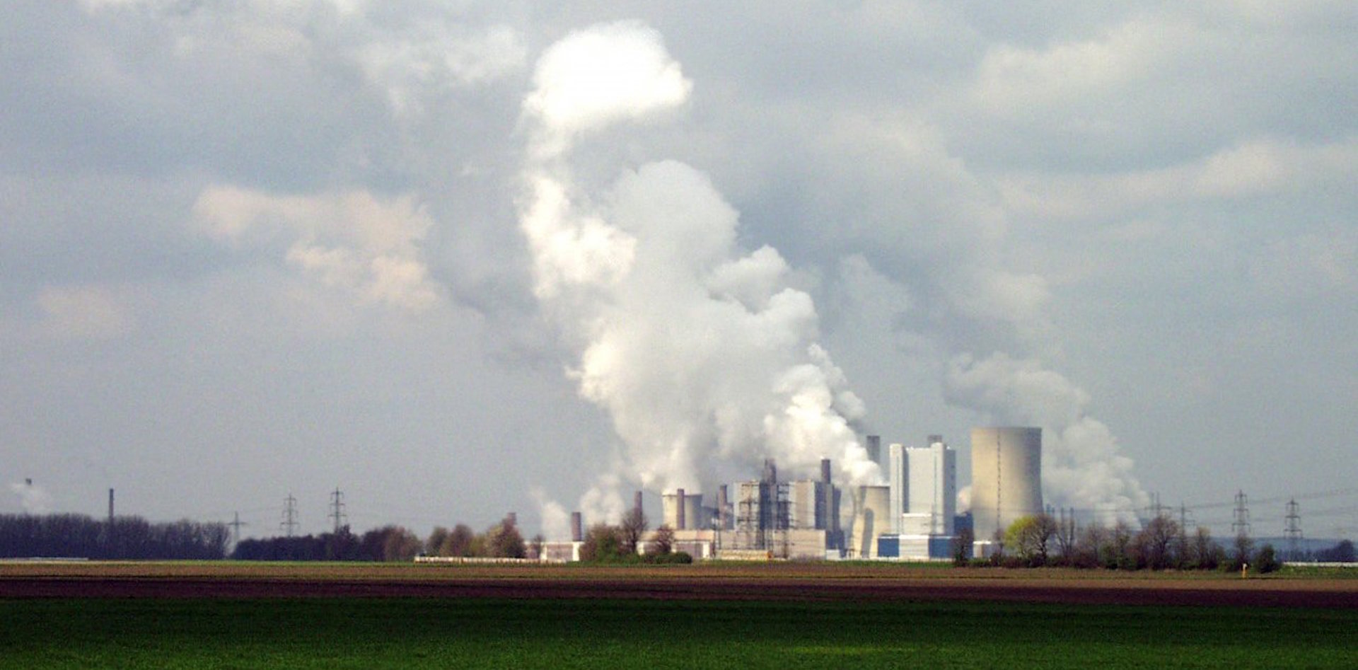A large coal plant seen from far away, with clouds of steam rising from it