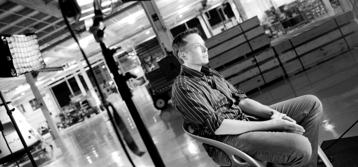 Elon Musk sitting in his office at Tesla, looking serious