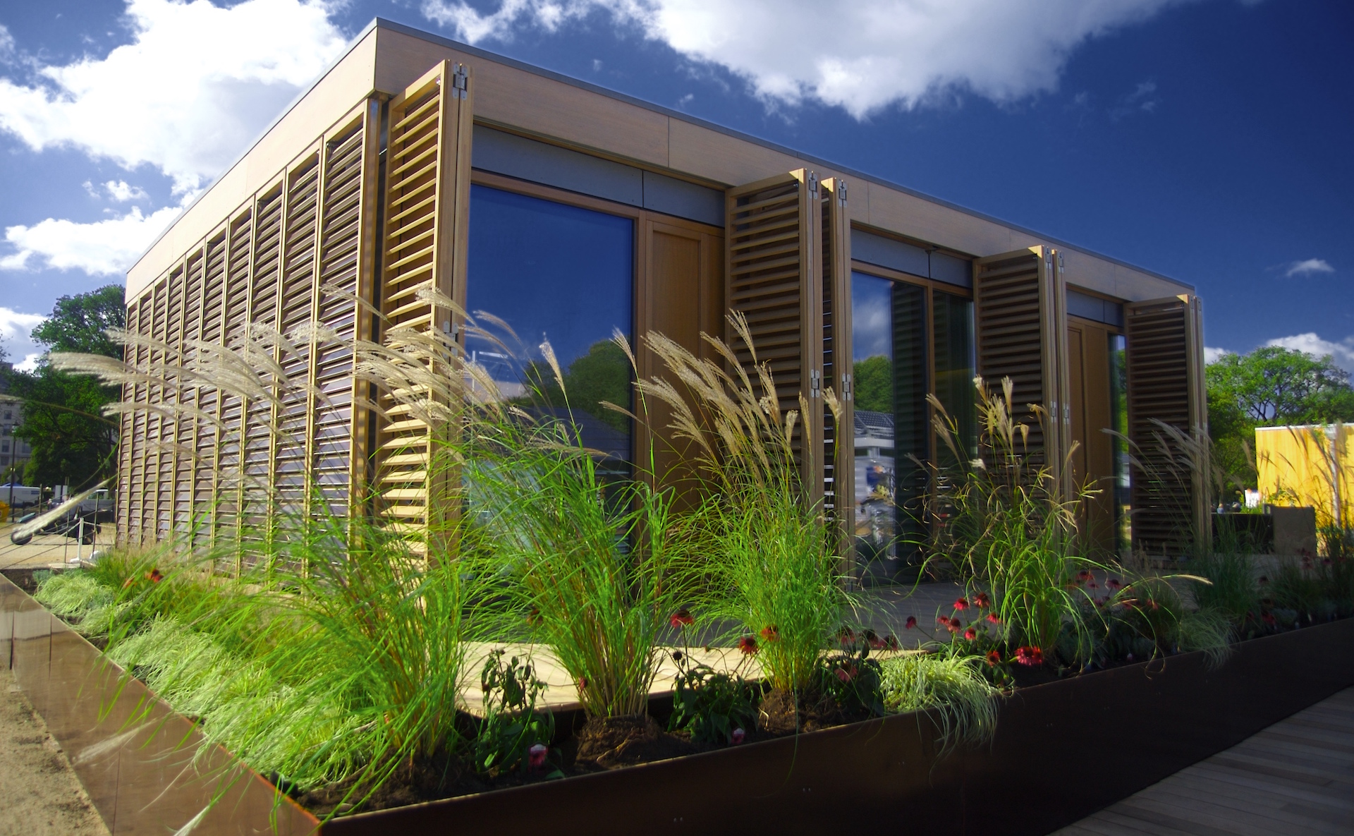 a small passive house building on Darmstadt University campus with a blue sky overhead and grasses growing in front of it