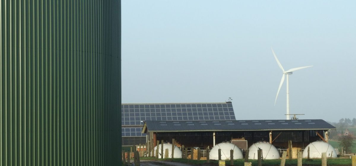 view of a farm with biogas, solar panels on the roof and a windmill in the background