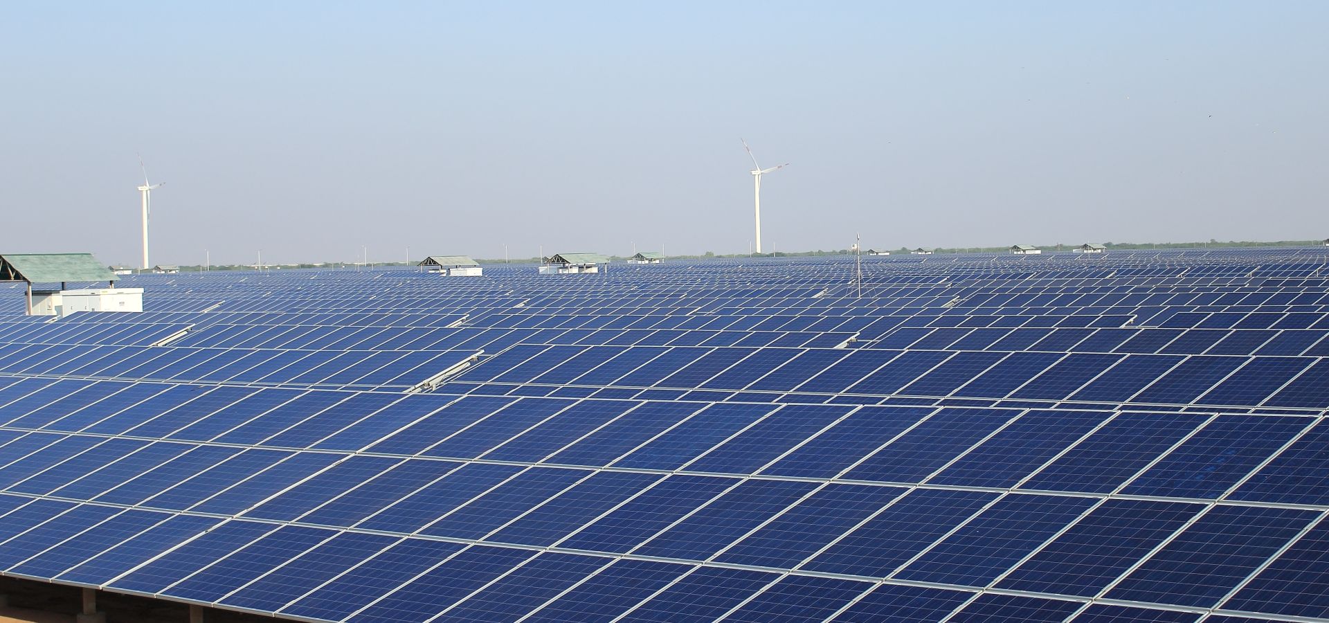 view of a field of solar panels with windmills interspersed