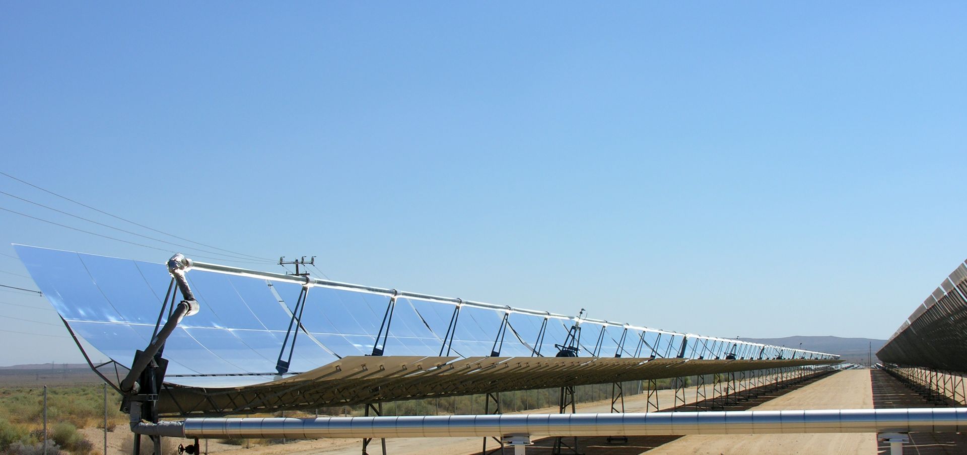 Solar trough reflecting a blue sky with desert in the background