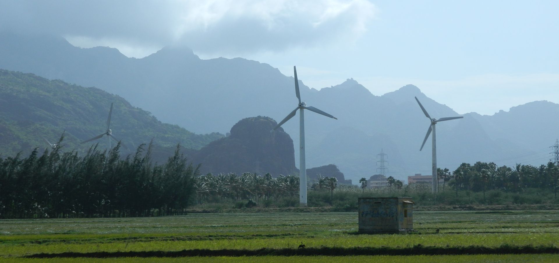 Windmills in a green field with low clouds and mountains in the background