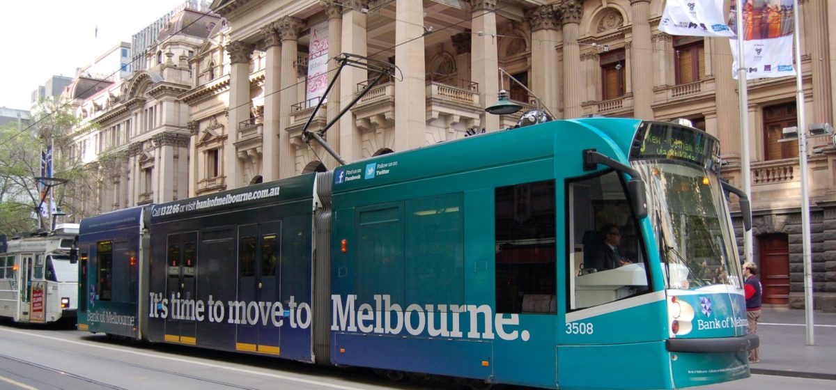 Photo of a tram in Melbourne by a historic building, with an advertisement reading "It's time to move to Melbourne" on the side