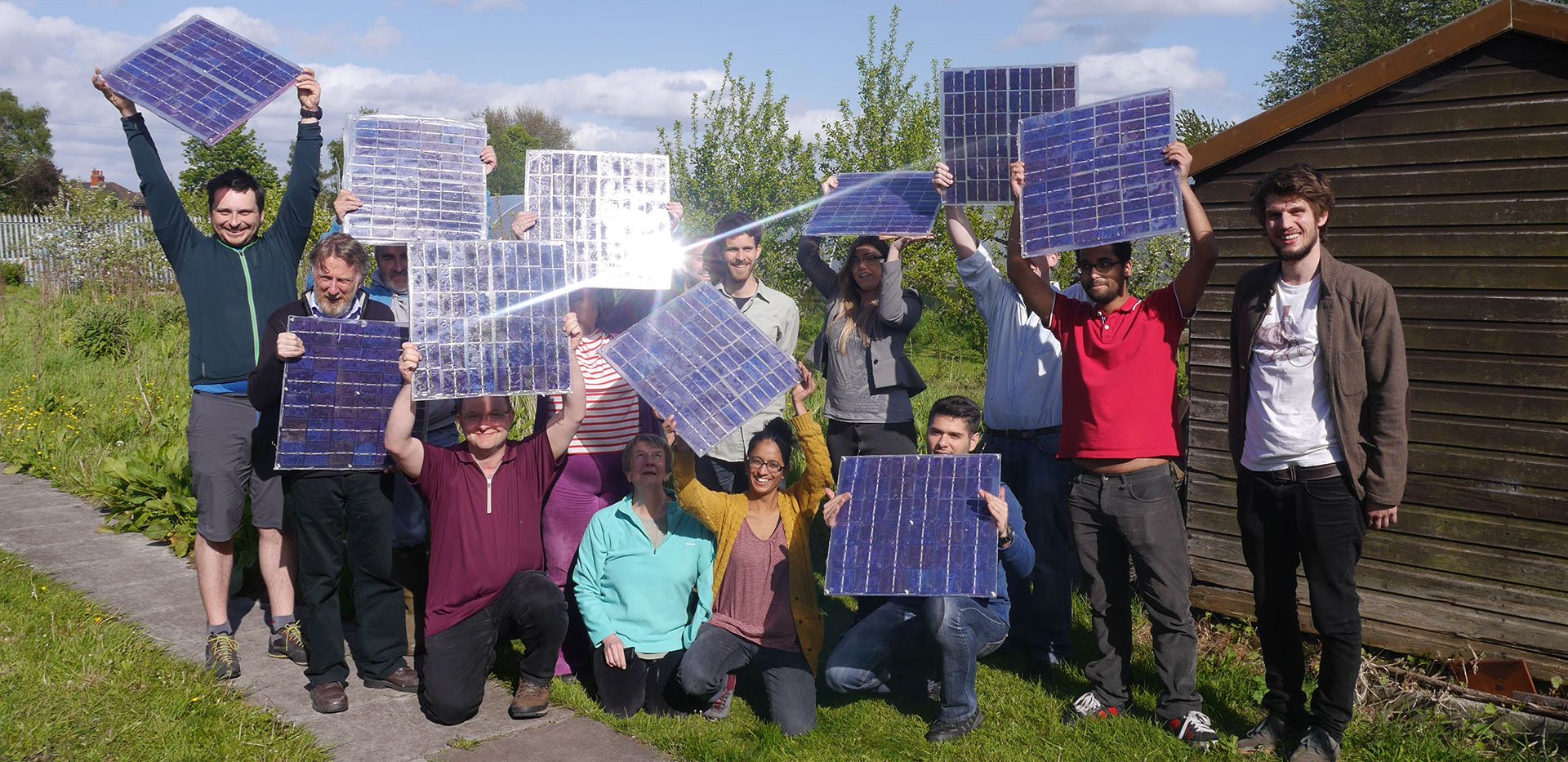 group of ten people of different ages holding solar panels up in the sunlight in a community garden