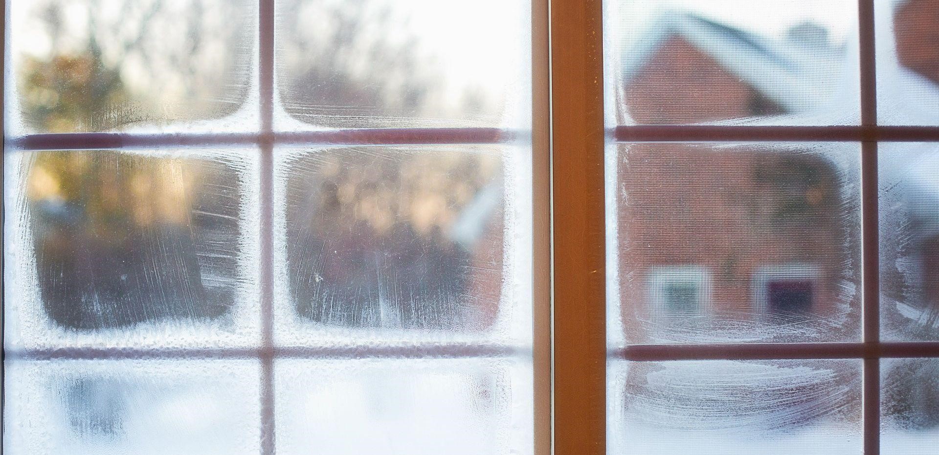 condensation on a window, with a snowy house seen outside
