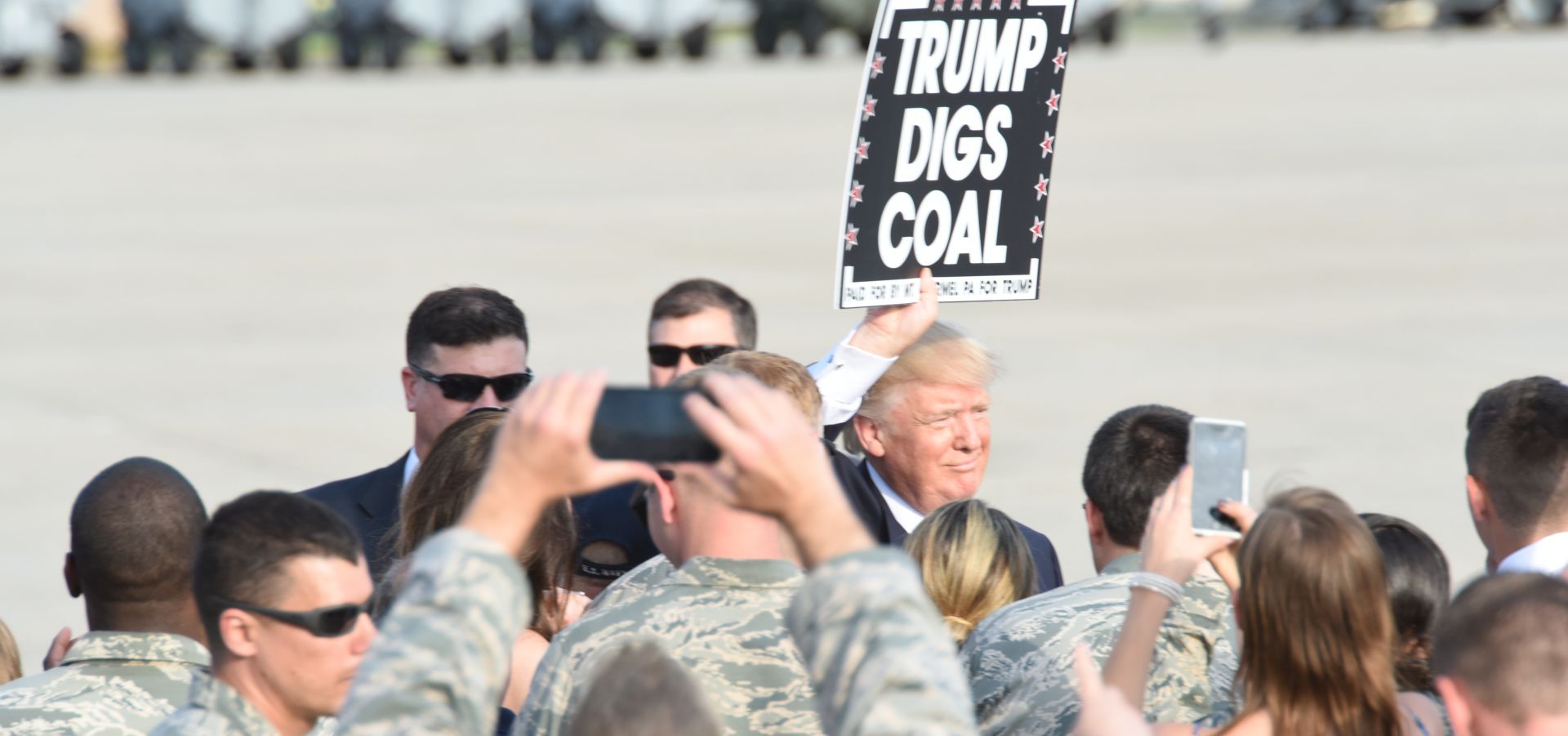 Trump holds a sign "Trump digs coal" surrounded by people taking pictures (U.S. Air National Guard Photo by Master Sgt. Culeen Shaffer/Released)