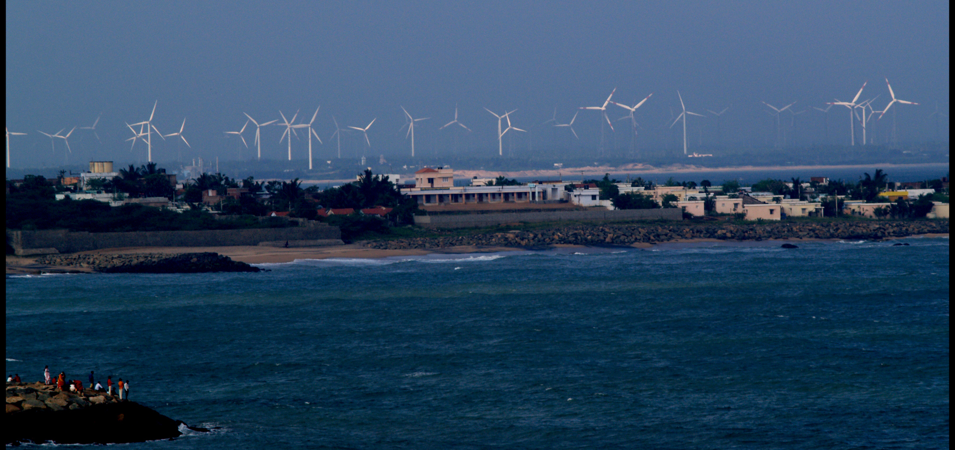 windmills seen from the coastline with people looking from an island