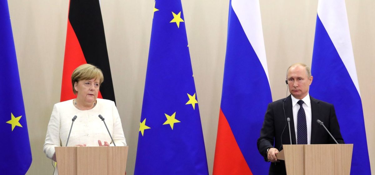 Angela Merkel and Vladimir Putin meet at Sochi with EU, Russian and German flags behind them
