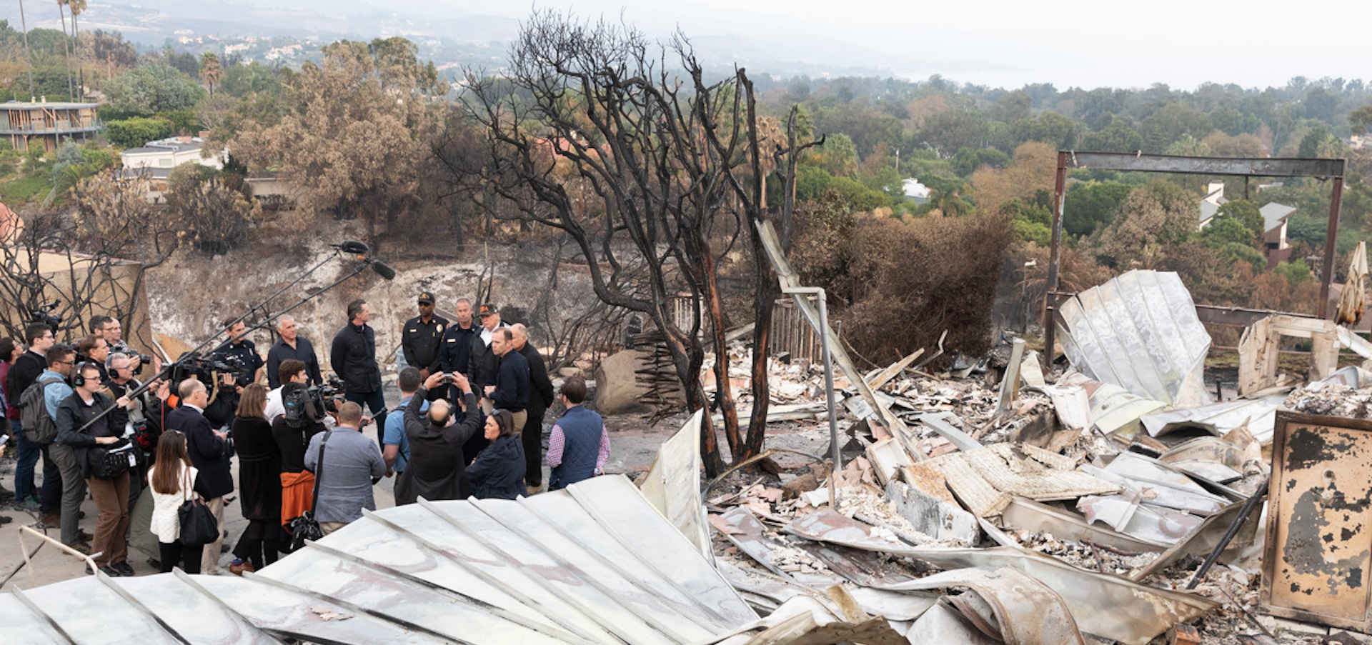 Trump and team stand in front of a collapsed, burned out building in california surrounded by smog